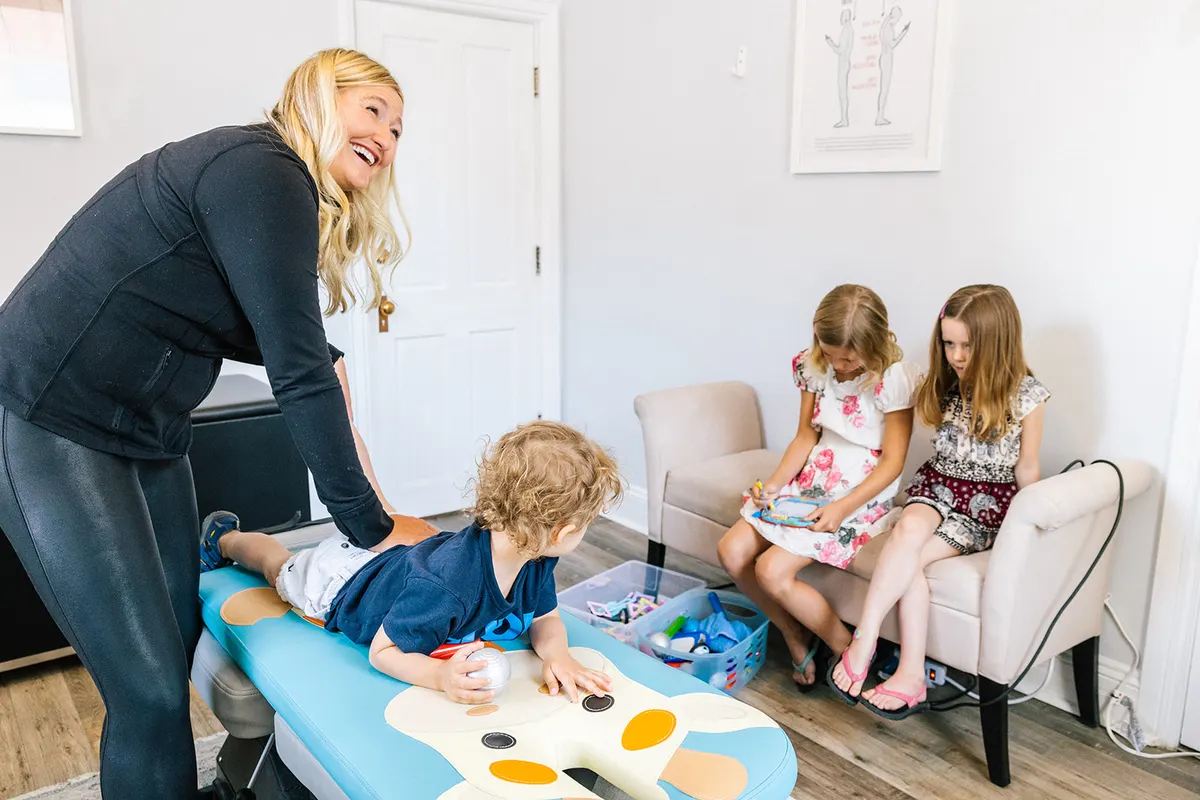 A toddler on the pediatric table with Dr. Kincaid while two older siblings wait nearby