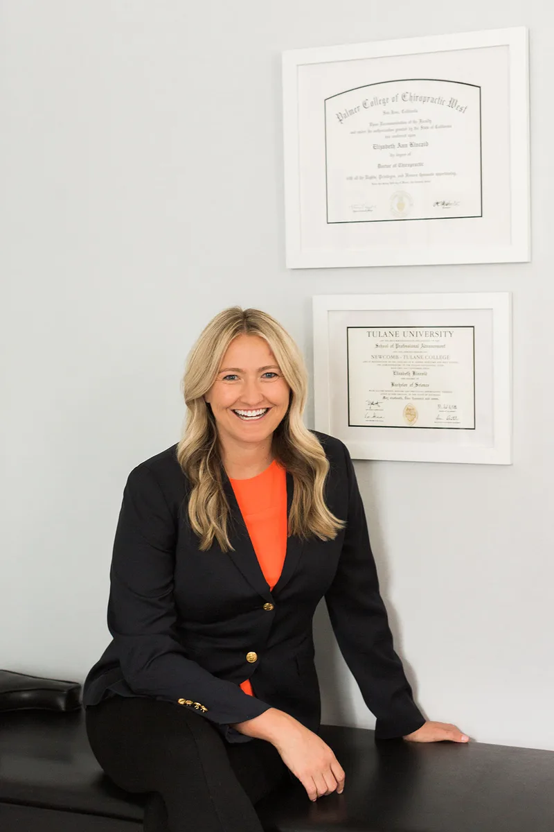 Dr. Elizabeth Kincaid in her office beside her Palmer College of Chiropractic West and Tulane University diplomas